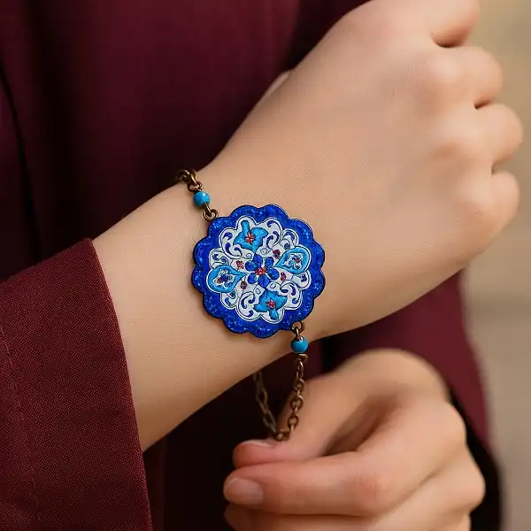 کلوزآپ دست یک فرد در حال نگه داشتن یک دستبند میناکاری شده با رنگ‌های آبی و قرمز